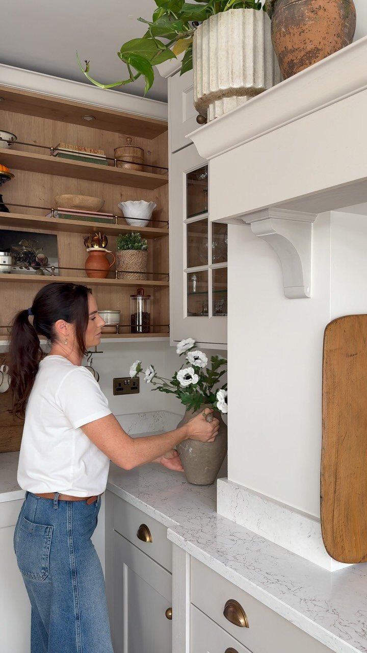 33 Kitchen Setting Ideas with Islands, Lighting, and Storage 2 Woman placing flowers on a kitchen counter next to wooden open shelving.