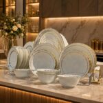 White and gold rimmed dinnerware set arranged on a white marble kitchen counter.