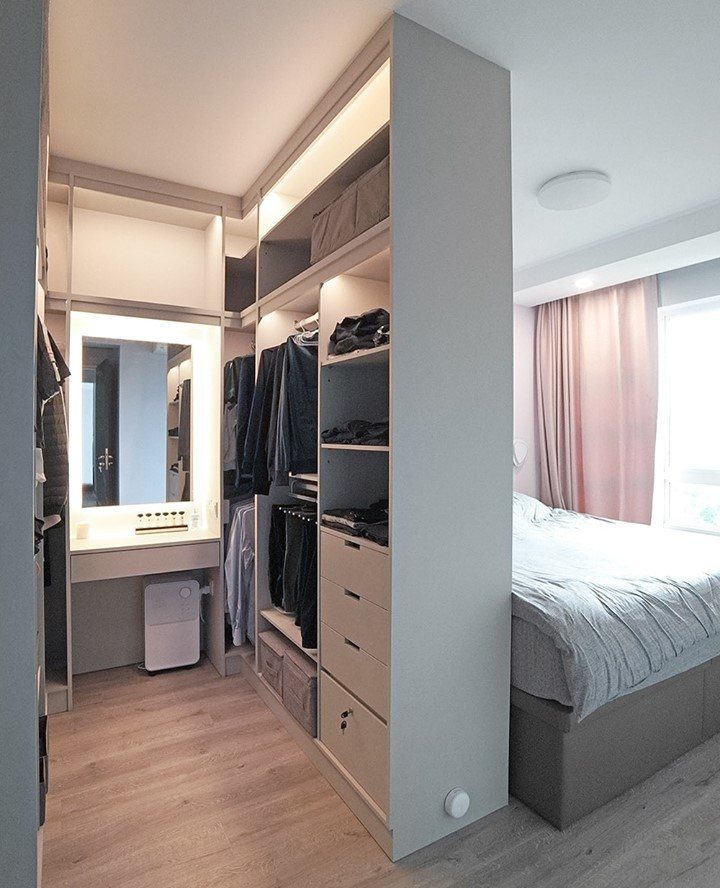 Modern walk-in closet layout with built-in shelving and vanity next to a bed.