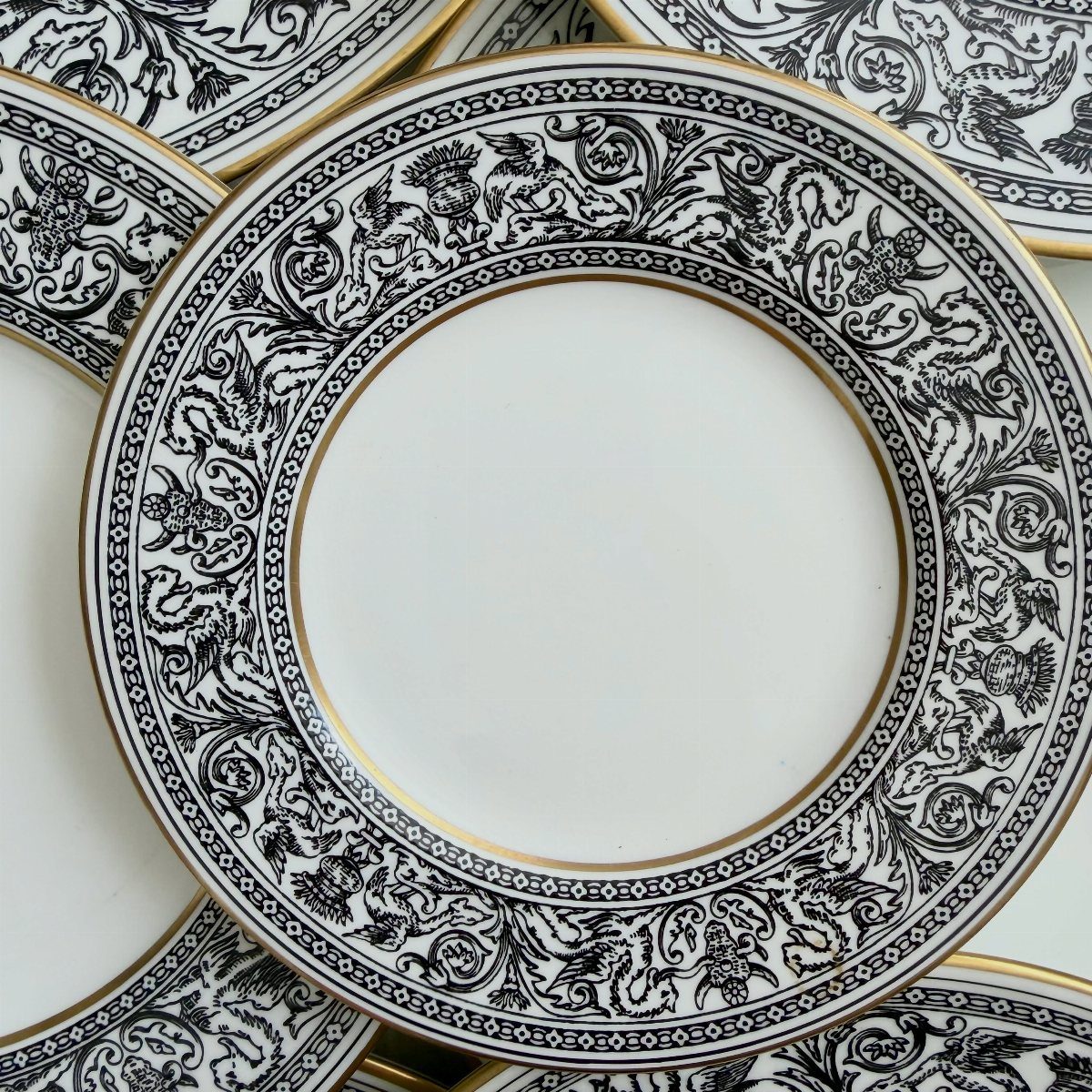 White porcelain plates with intricate black ornate patterns and gold gilded rims.