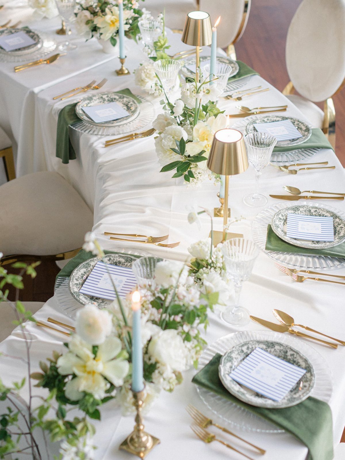 Dining table set with white flowers, gold cutlery, and light blue taper candles.