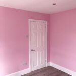 Bright pink painted walls in a room with a white door and grey flooring