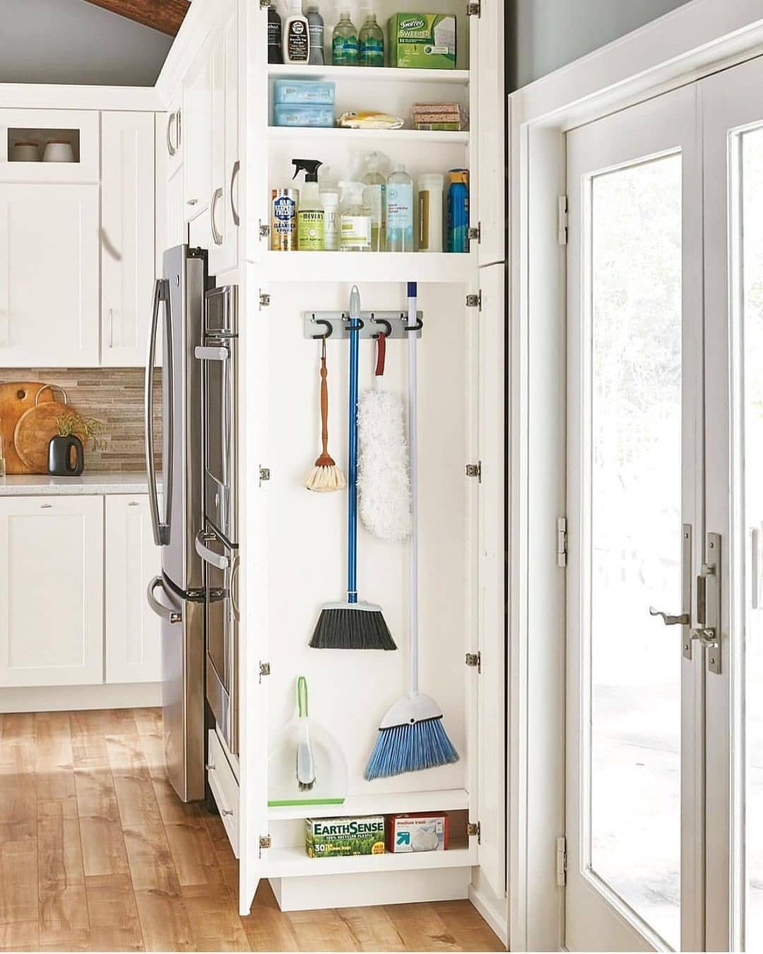 10 Broom Closet Design Ideas for Laundry Rooms and Stairs 9 White built-in storage cabinet with cleaning supplies and hanging brooms in a kitchen.
