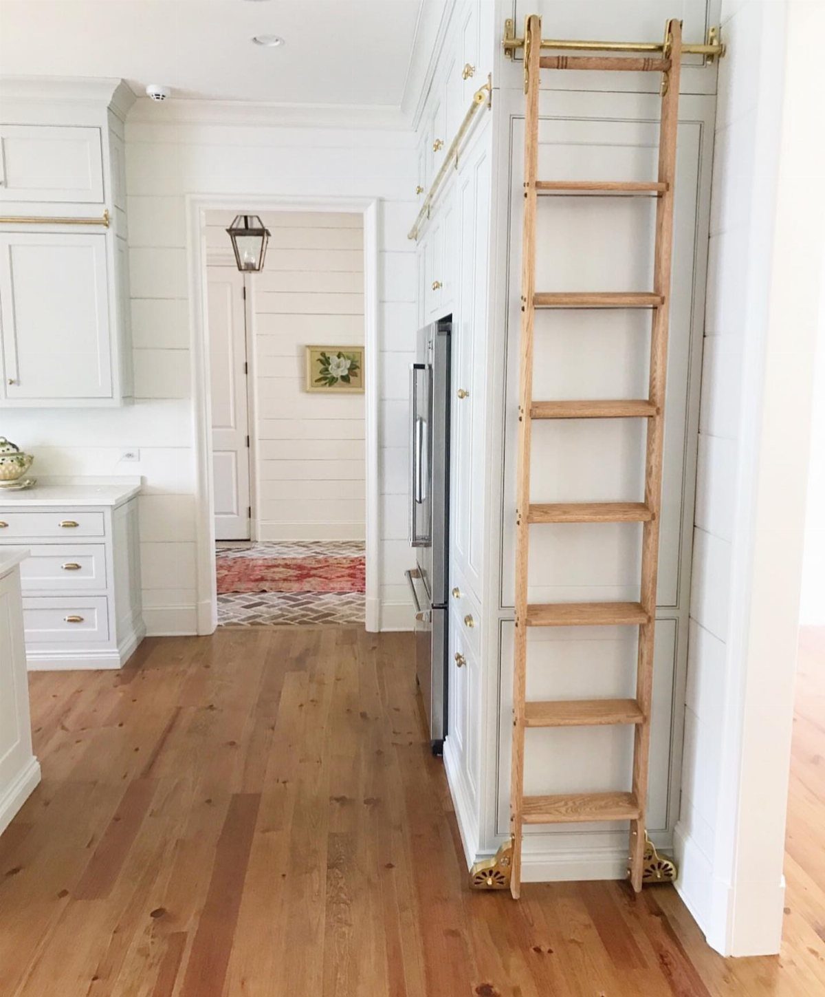 33 Kitchen Setting Ideas with Islands, Lighting, and Storage 18 Wooden rolling ladder on a brass rail against tall white kitchen cabinets