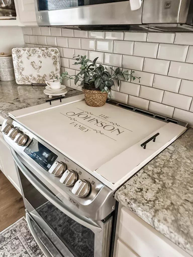 White personalized tempered-glass stove cover protecting a stainless steel oven range in a kitchen.