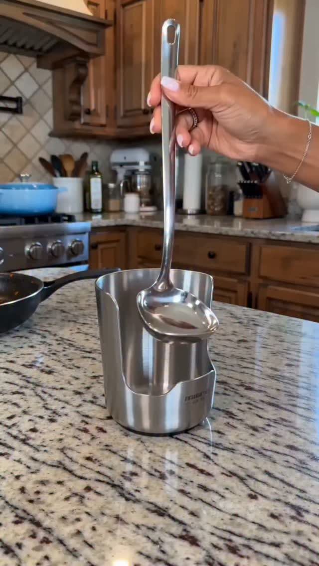 Silver metal ladle being placed into a stainless steel kitchen gadget storage holder.