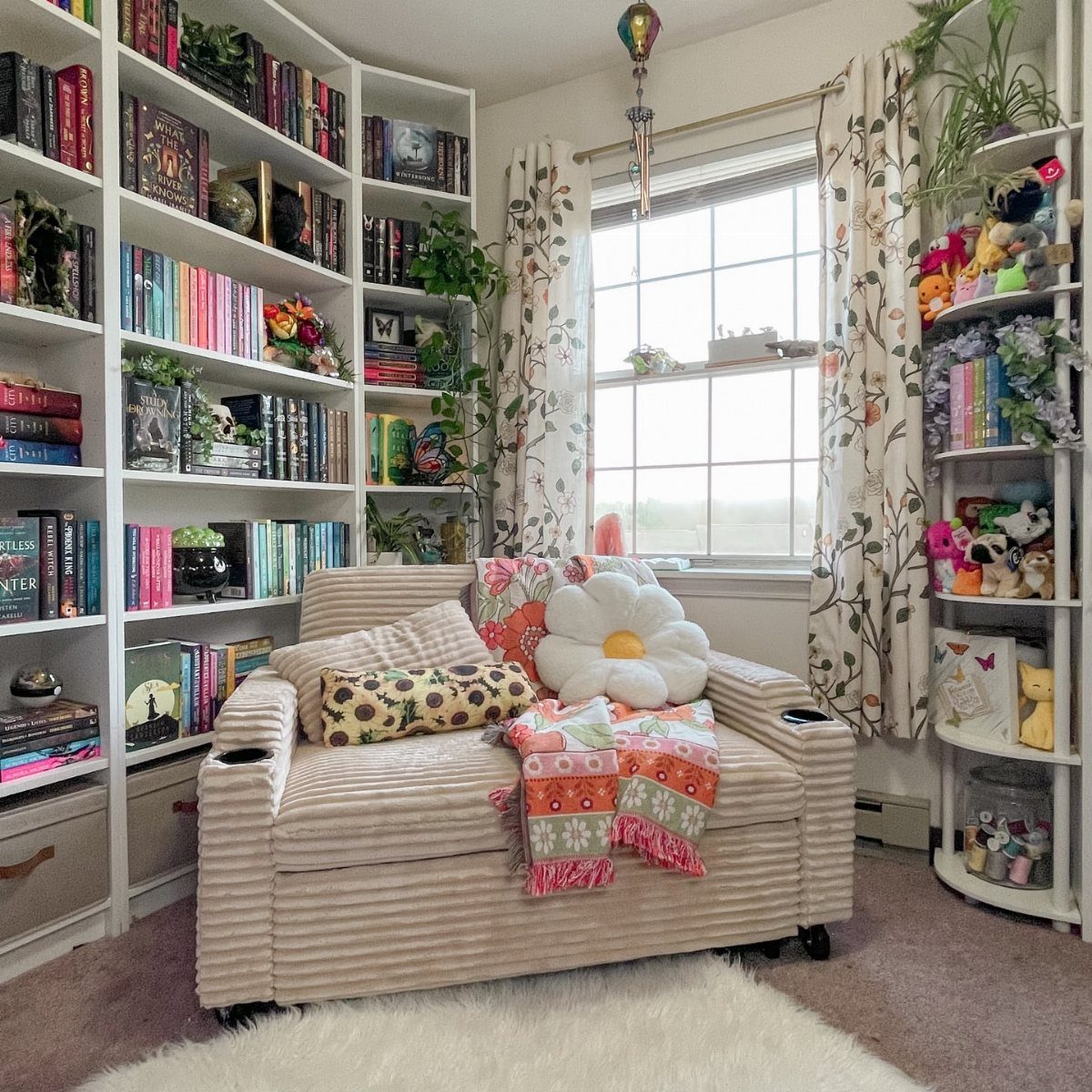 Beige ribbed armchair with colorful pillows and a blanket next to a white bookshelf.