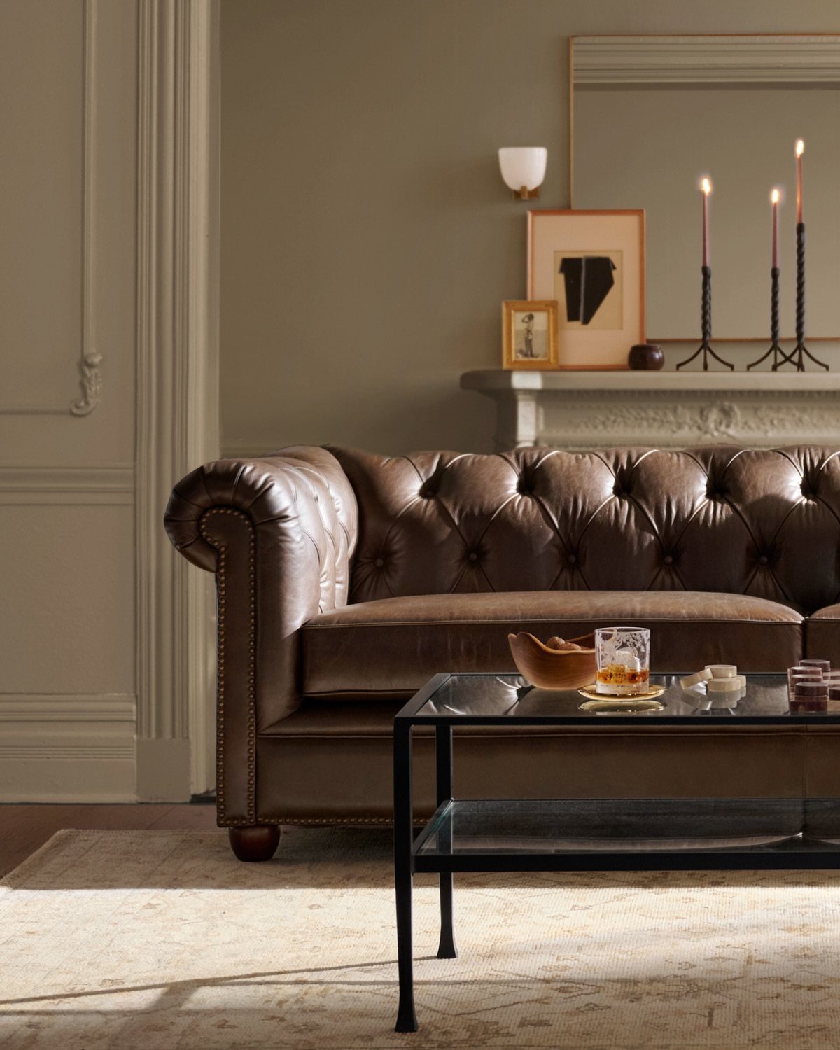 Brown leather Chesterfield sofa in a cozy living room with candles and art.