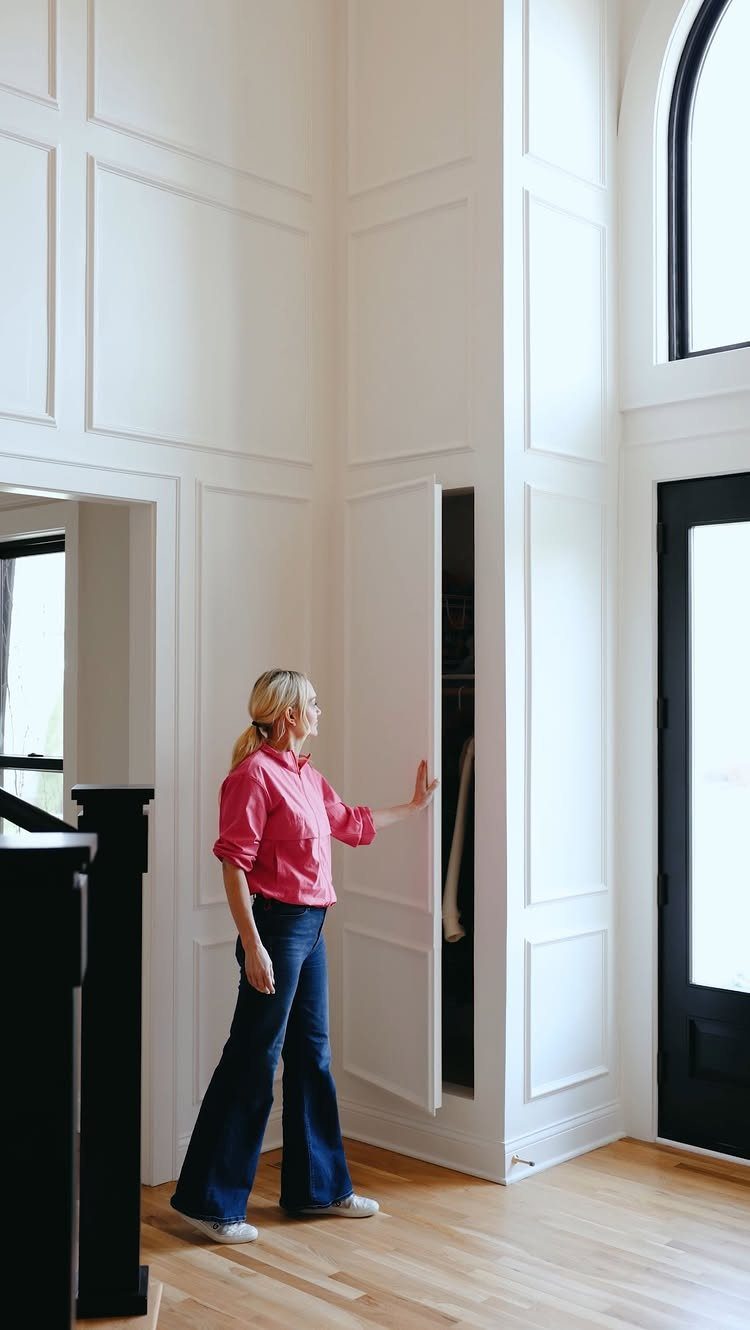 10 Broom Closet Design Ideas for Laundry Rooms and Stairs 2 Woman opening a disguised closet door that blends into white wall paneling.