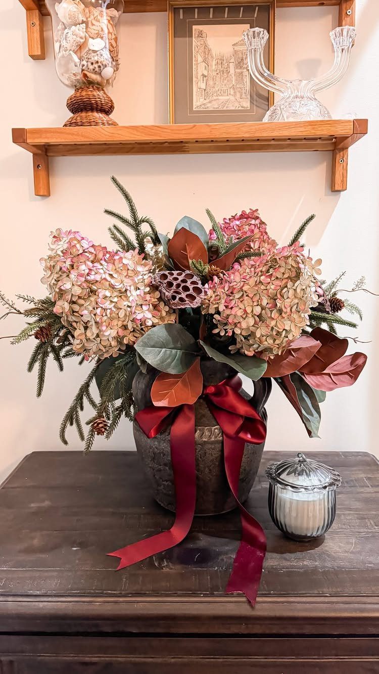 Dried pink hydrangeas and greenery in a metal vase with a red ribbon.