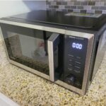 Stainless steel microwave oven with digital display on a granite kitchen countertop.
