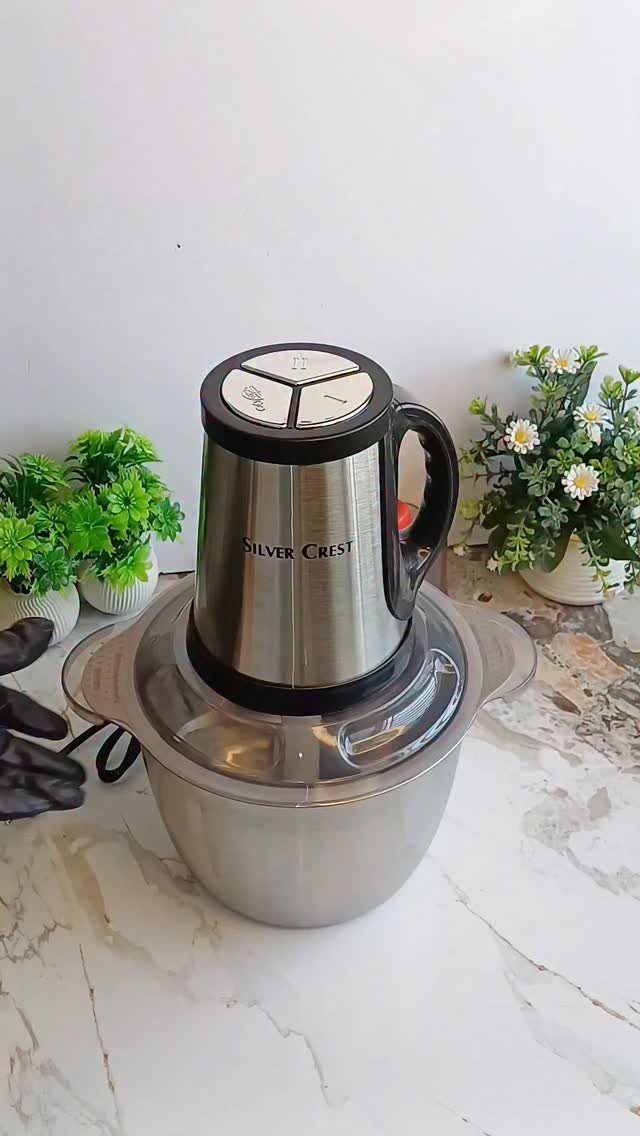 Silver Crest electric food processor on a white marble countertop with small plants.