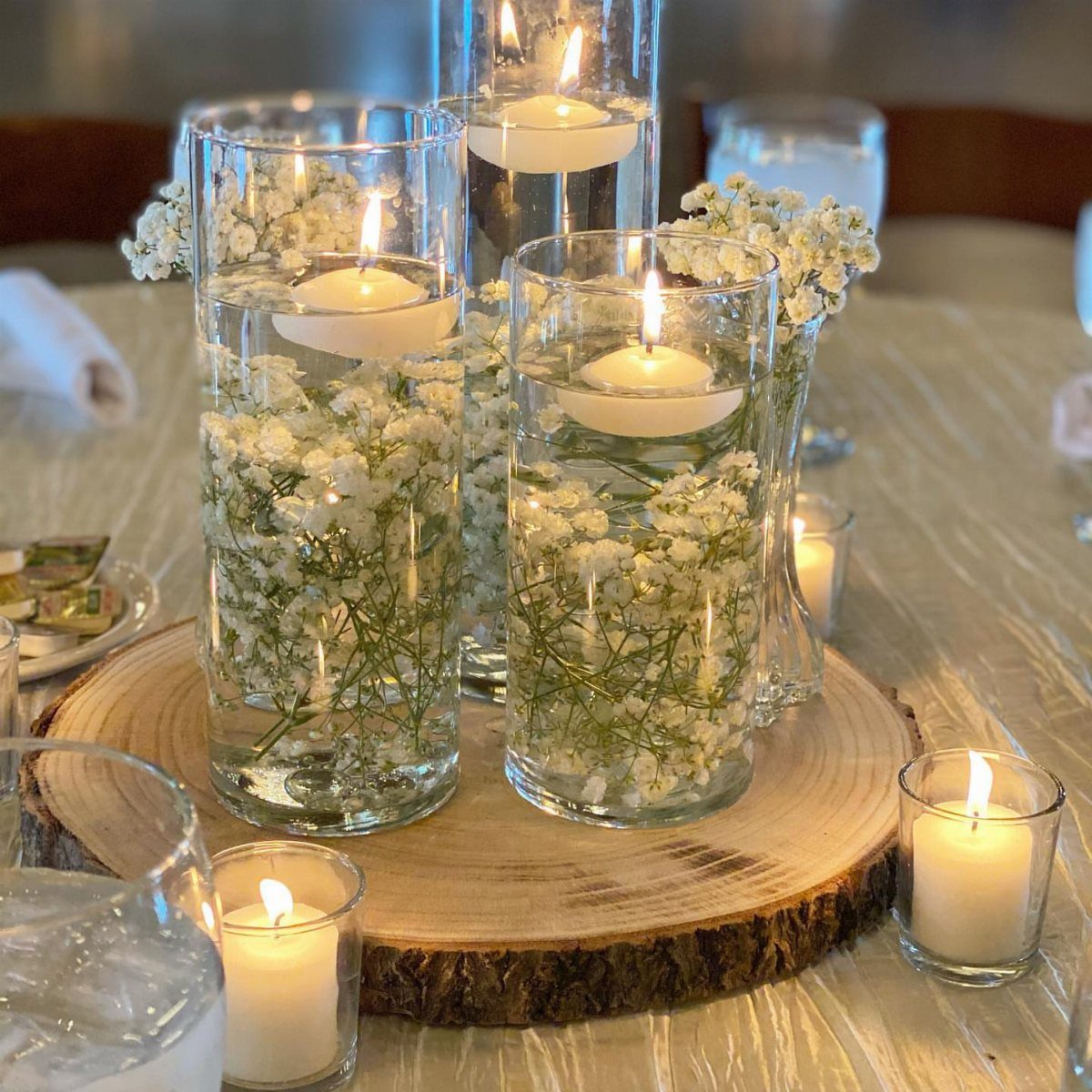 26 Table Toppers Wedding Ideas, From Candlelit to Tropical 22 Floating white candles and baby's breath flowers in glass cylinders on a wood slice.