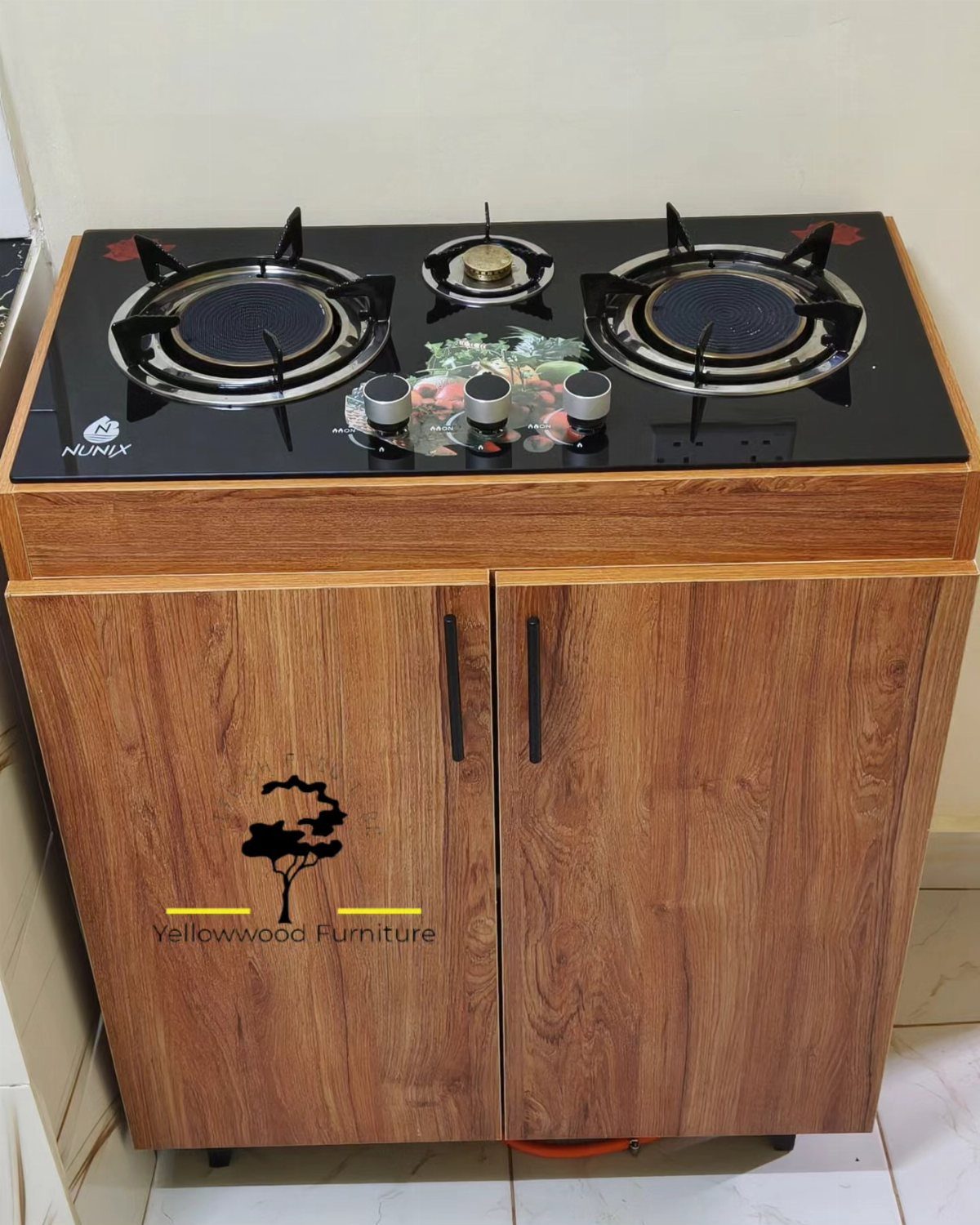 Gas cooker integrated into a wooden cabinet with two doors and a black glass top.