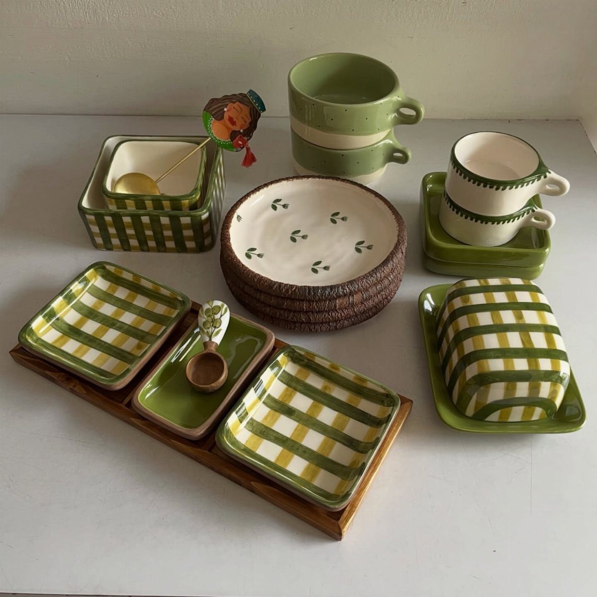 Green and white ceramic kitchenware including mugs, plates, and checkered bowls on white surface