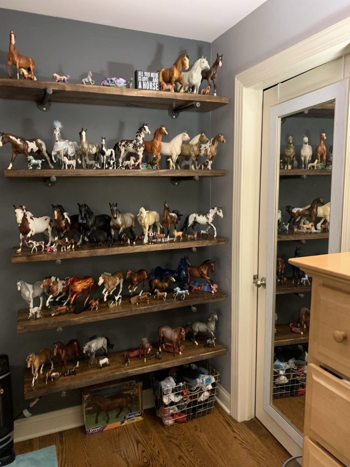 Horse figurines displayed on rustic wooden floating shelves against a grey bedroom wall.