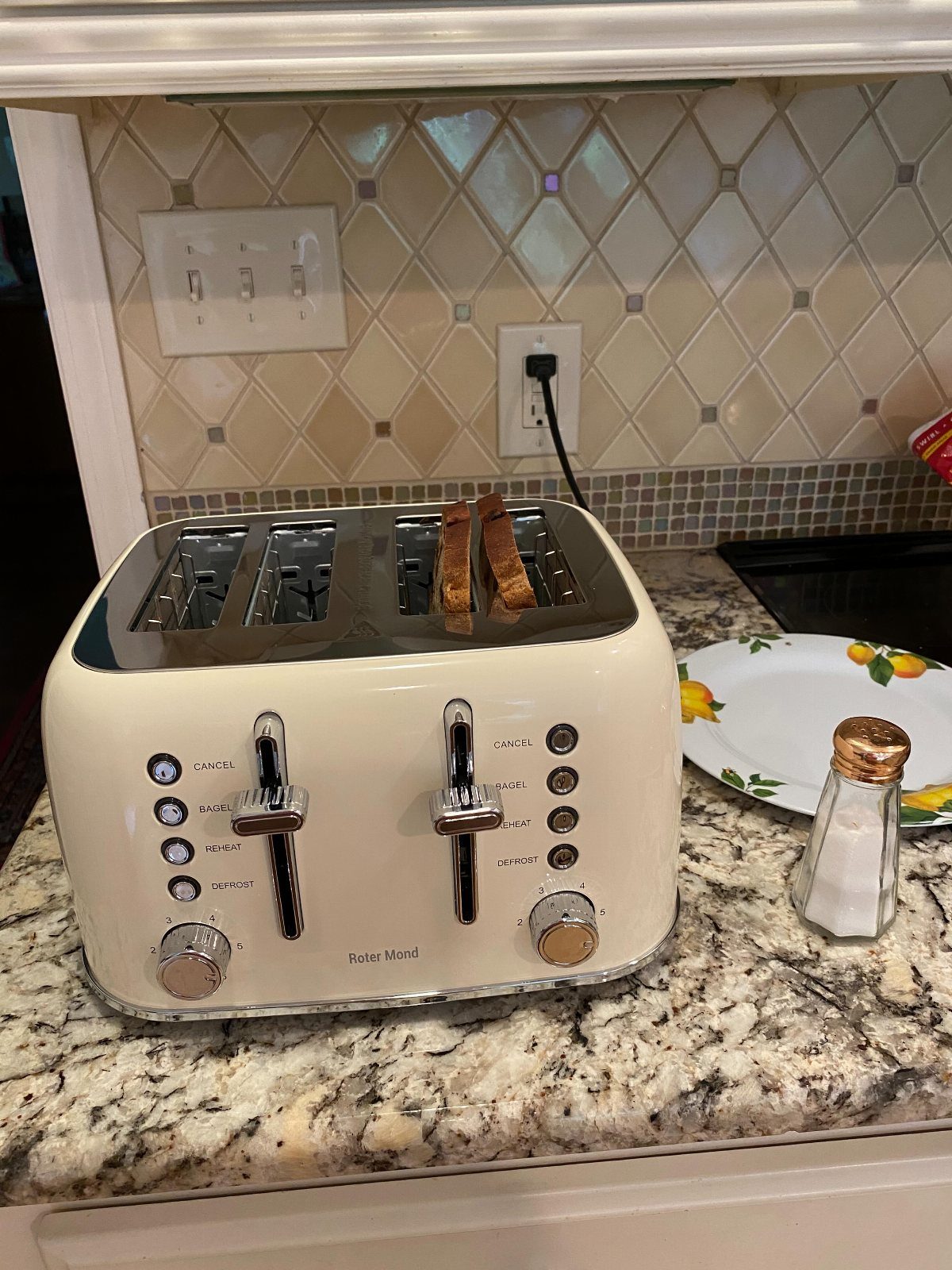 Cream-colored four-slice toaster on a granite countertop with toasted bread popping up.