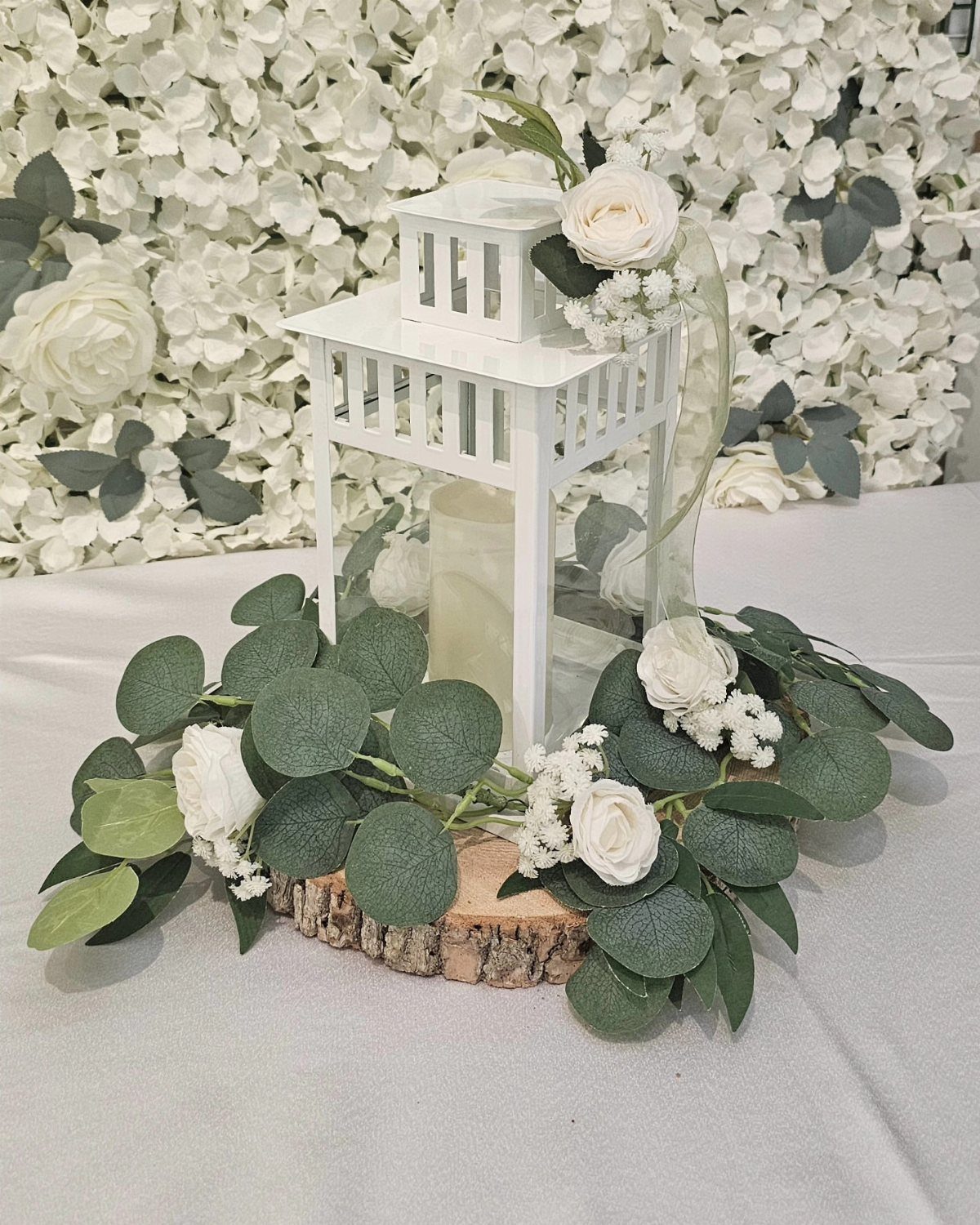 26 Table Toppers Wedding Ideas, From Candlelit to Tropical 16 White decorative lantern with candle on wood slice surrounded by eucalyptus and roses.
