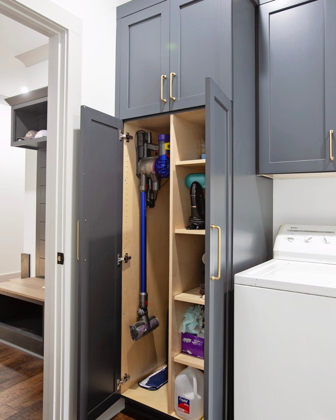 10 Broom Closet Design Ideas for Laundry Rooms and Stairs 3 Grey built-in broom closet containing a vacuum and cleaning supplies next to a washer.