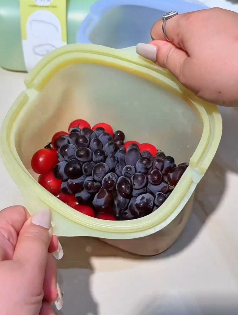 17 Kitchen Snack Storage Ideas for Pantries and Counters 16 Yellow silicone storage container filled with red and purple grapes on a white counter.