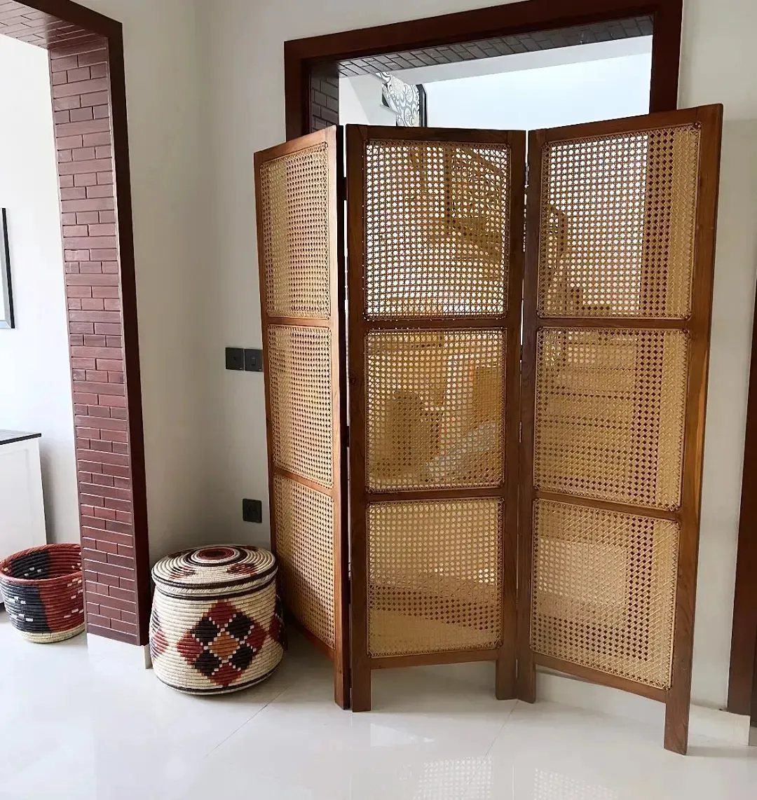 Three-panel wooden room divider with woven cane inserts in a bright interior room.