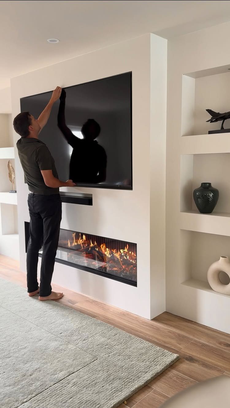 16 TV Designs for Living Room Walls, Units and Mounts 12 Man adjusting a large flat-screen TV mounted above a modern linear fireplace.