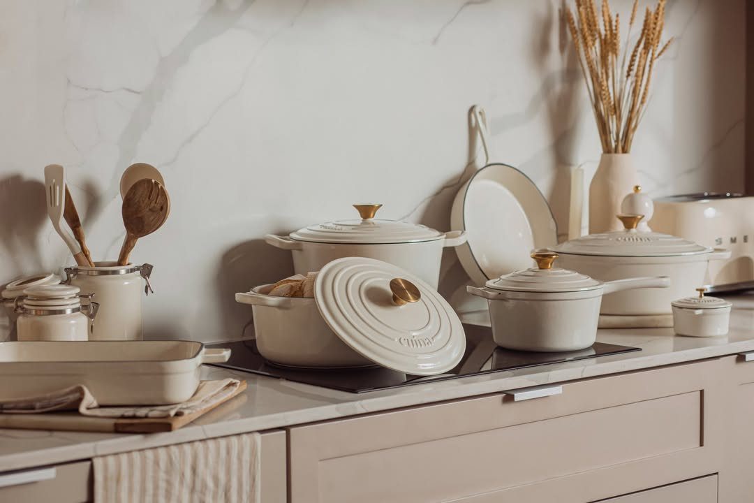 Cream-colored cookware set including pots and pans on a modern kitchen stovetop.