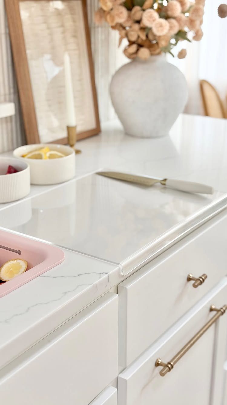 White veined quartz countertop with integrated cutting board and white kitchen cabinetry.