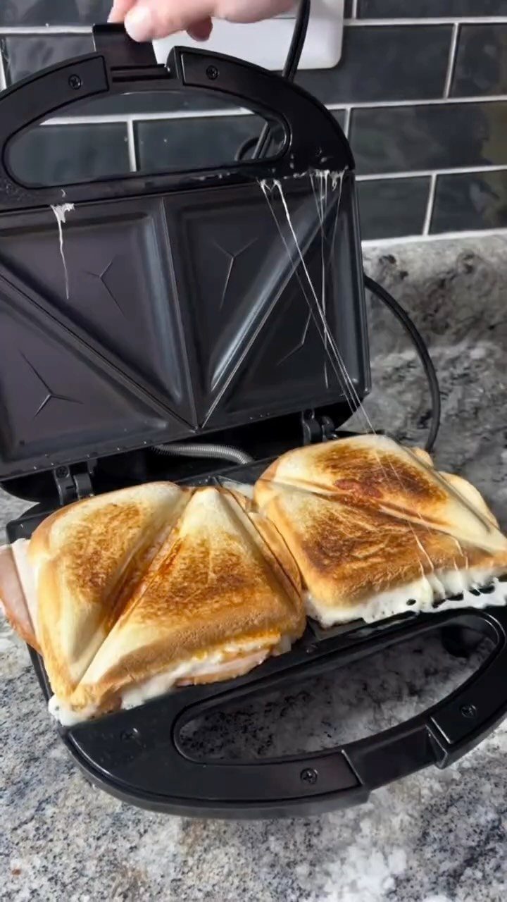 Two toasted grilled cheese sandwiches inside an open black electric sandwich press.