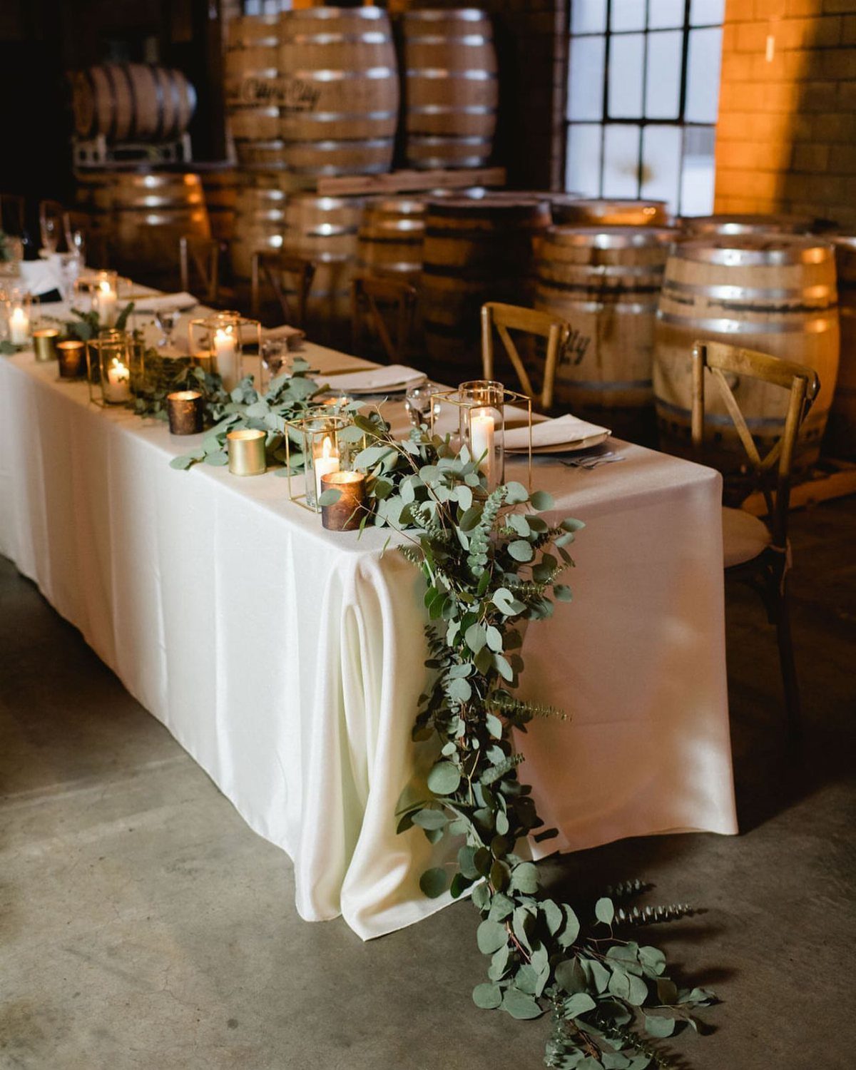 Silver dollar eucalyptus garland with candles on a white tablecloth in a rustic room.