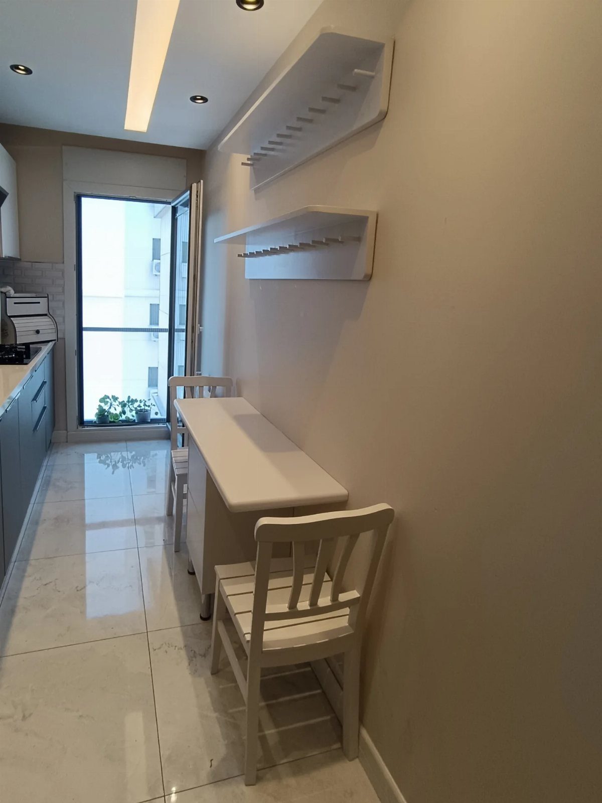 11 Kitchen Breakfast Table Ideas for Small and Roomy Kitchens 3 Narrow white rectangular table with two matching chairs against a beige kitchen wall.