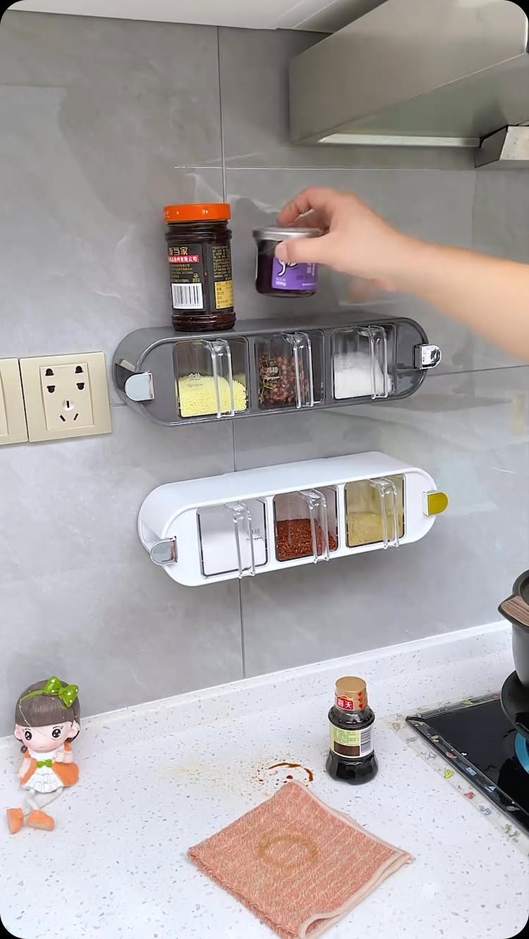 Wall-mounted plastic spice organizers with clear lids on a grey tiled kitchen wall.