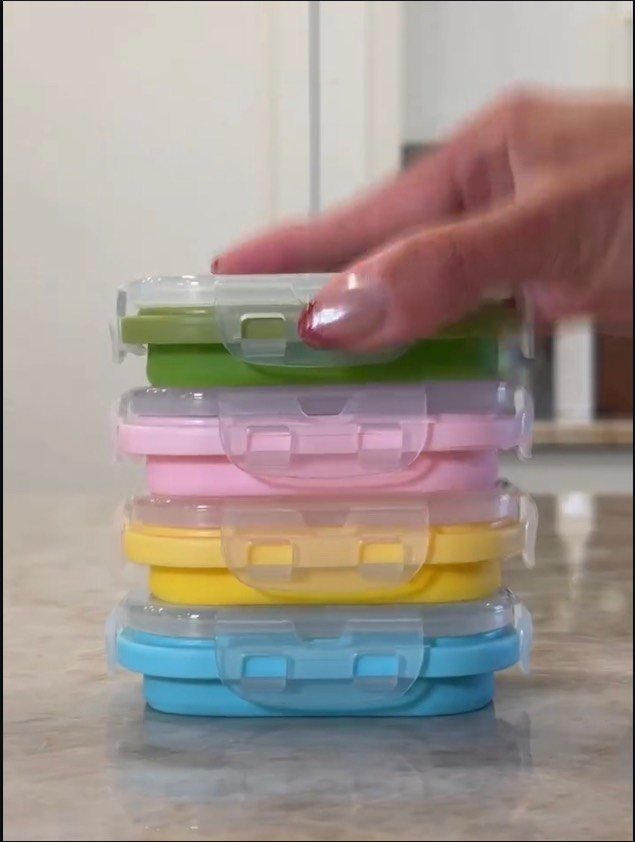 17 Kitchen Snack Storage Ideas for Pantries and Counters 14 Stacked colorful plastic snack containers on a granite countertop with a hand reaching.