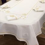 White table runner with gold embroidery layered over a matching white tablecloth.