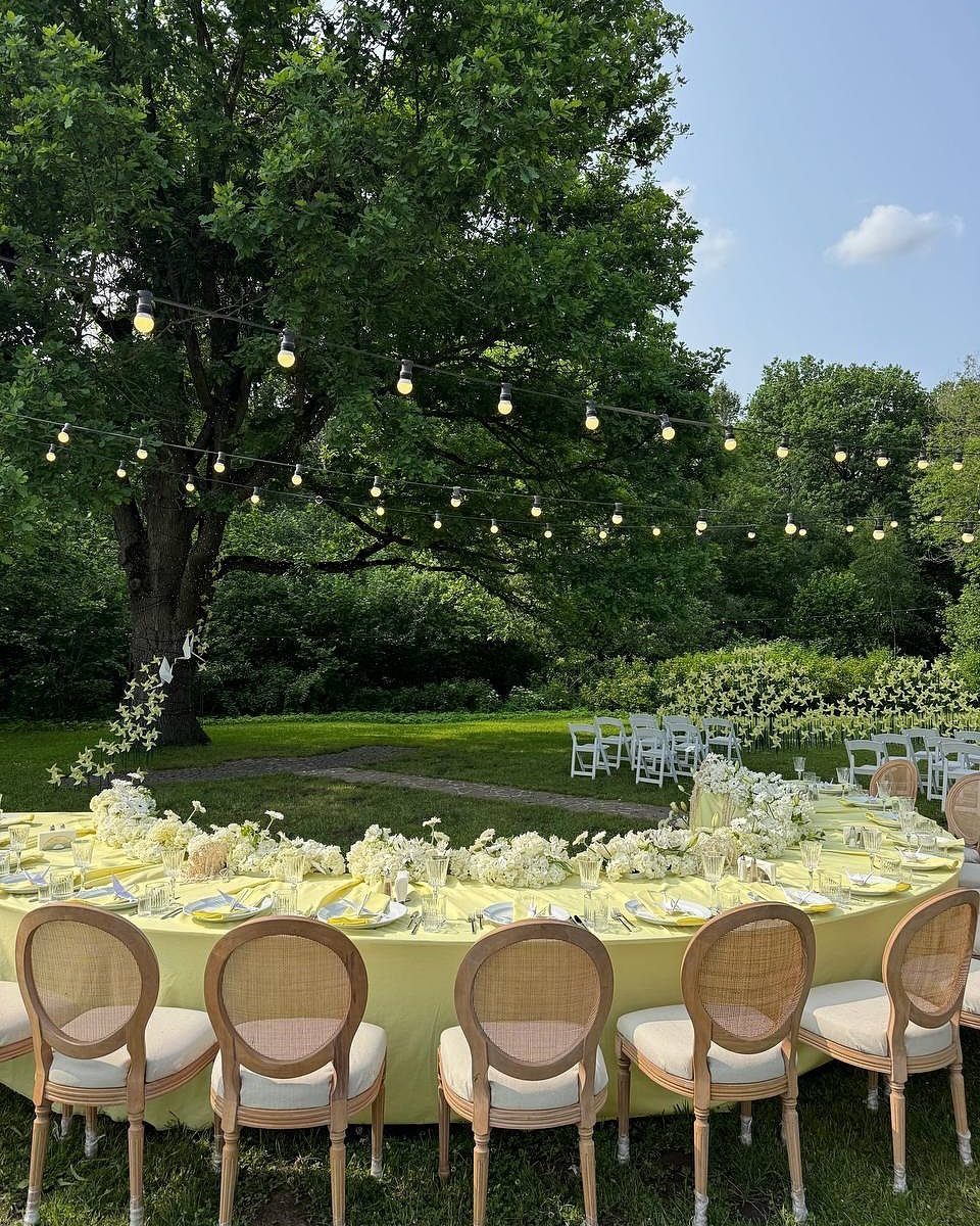 28 Wedding Decorations Ideas at Home with Flowers and Lights 19 Long yellow wedding table with white flowers and wicker chairs under garden string lights.