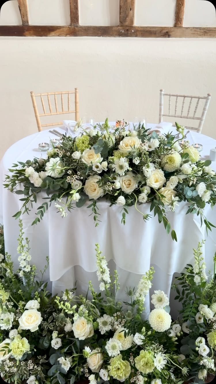 26 Table Toppers Wedding Ideas, From Candlelit to Tropical 6 White rose and greenery floral centerpiece on a white wedding table with matching base.