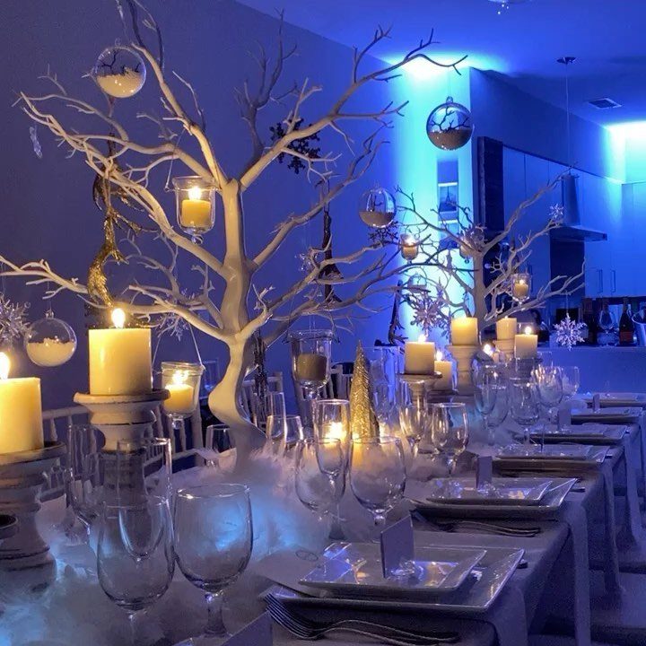 Winter themed Christmas dinner table with white branches, candles, and blue ambient lighting