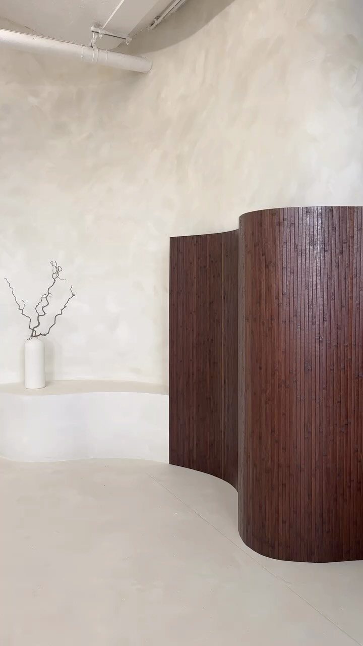 Curved dark brown wooden slat room divider in a minimalist white interior space.